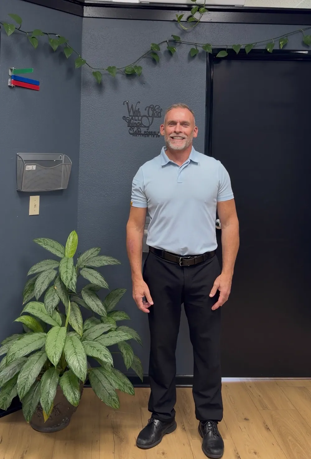 Dr. Steve Van Laecken DC standing in the SpinalWorks Chiropractic clinic next to a wall sign reading With God All Things Are Possible, Matthew 19:26